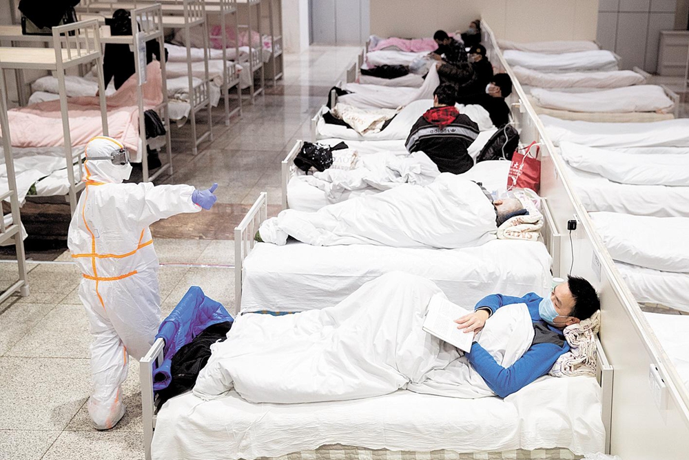 2月5日晚，入住武汉国际会展中心方舱医院的患者躺在病床上安静地看书，一旁经过的协和医院护士向他竖起大拇指。 （湖北日报全媒记者 柯皓 摄）.jpg